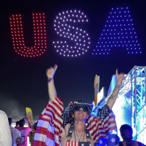 An attendee of Barefoot Country Music fest pictured underneath a particularly patriotic drone display. Taken from @barefootcountrymusicfest on Instagram.